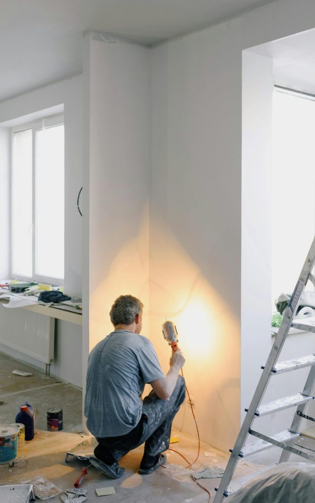 Back view of anonymous male in dirty clothes renovating walls in home while holding lamp